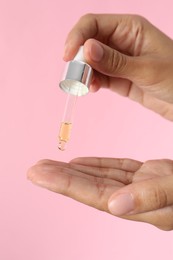 Photo of Woman applying cosmetic serum onto her finger on pink background, closeup