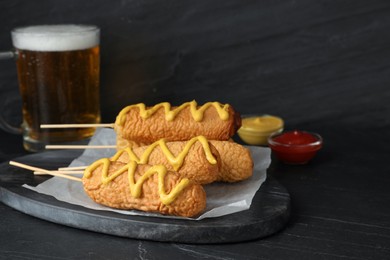 Photo of Delicious deep fried corn dogs with mustard on black table