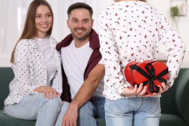 Photo of Little girl presenting her parents with gift at home