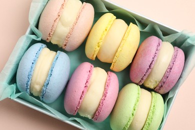 Many delicious colorful macarons in box on pink background, top view