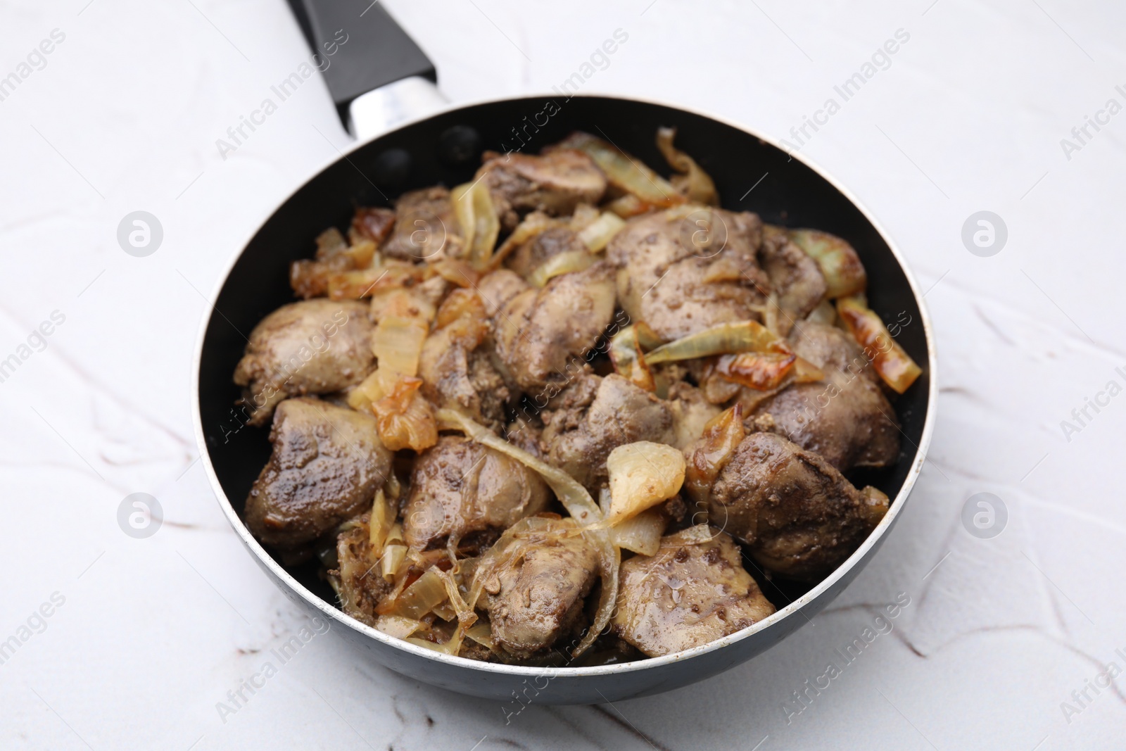 Photo of Pan with tasty fried chicken liver and onion on white textured table, closeup