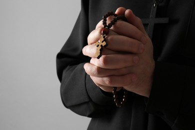 Photo of Priest with rosary beads praying on grey background, closeup. Space for text