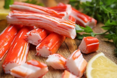 Photo of Delicious crab sticks with lemon on wooden board, closeup