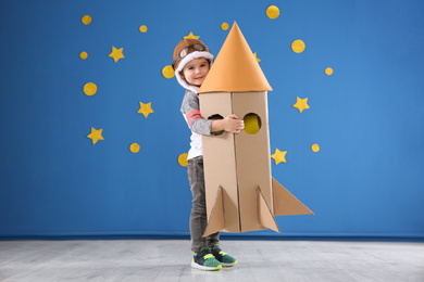 Photo of Cute little child playing with cardboard rocket near blue wall
