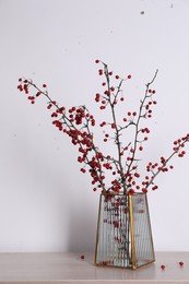 Photo of Hawthorn branches with red berries in vase on wooden table indoors