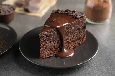 Photo of Pouring chocolate sauce onto delicious fresh cake on grey table, closeup