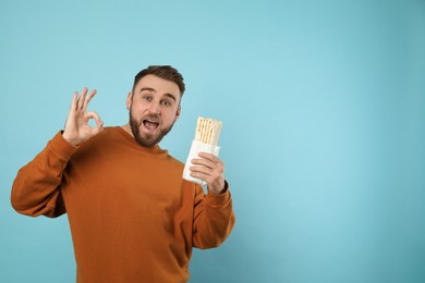 Photo of Excited young man with delicious shawarma on turquoise background, space for text