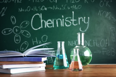Photo of Laboratory glassware and books on table near chalkboard. Chemistry concept