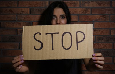 Photo of Abused young woman with sign STOP near brick wall. Domestic violence concept