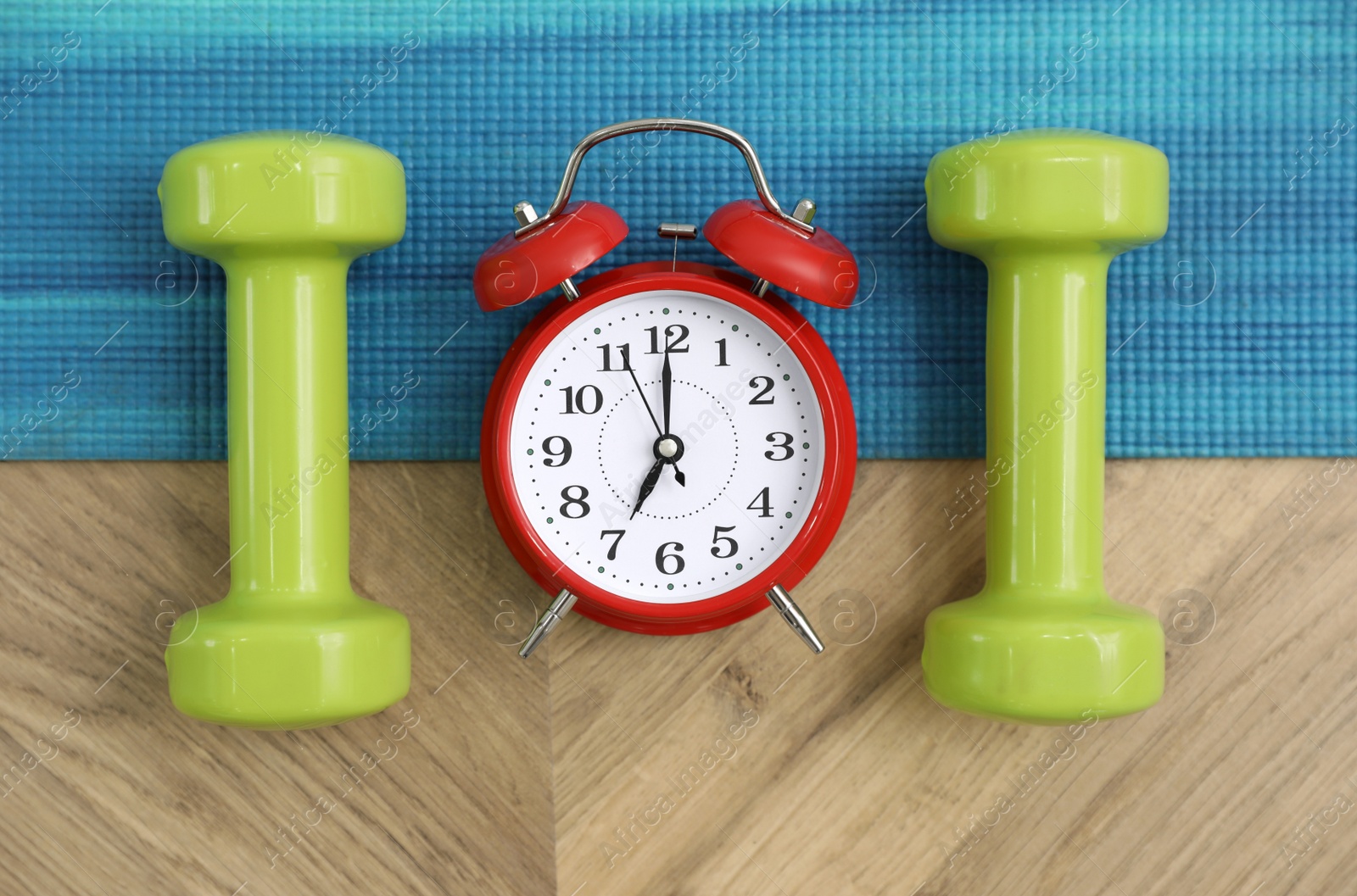 Photo of Alarm clock, yoga mat and dumbbells on wooden background, flat lay. Morning exercise