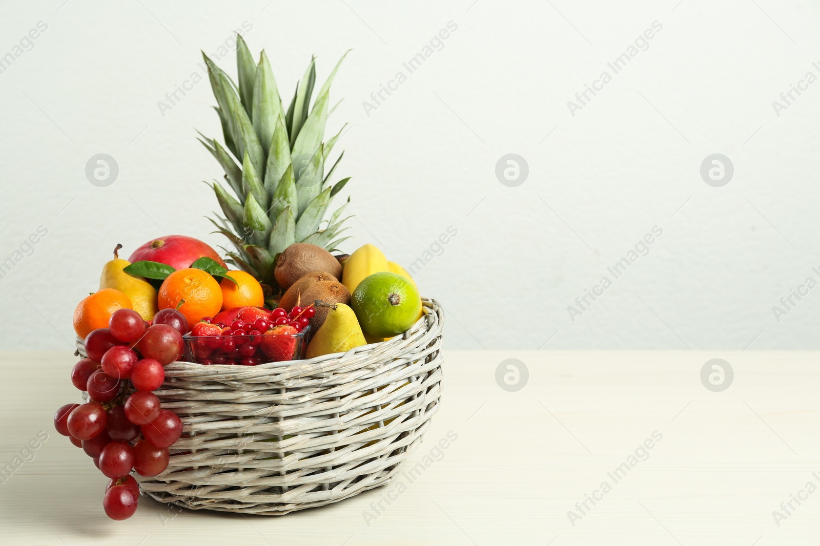 Photo of Wicker basket with different fresh fruits on white wooden table. Space for text