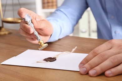 Male notary sealing document at table in office, closeup