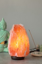 Himalayan salt lamp, buddha figure, incense and crystals on stone table near grey wall