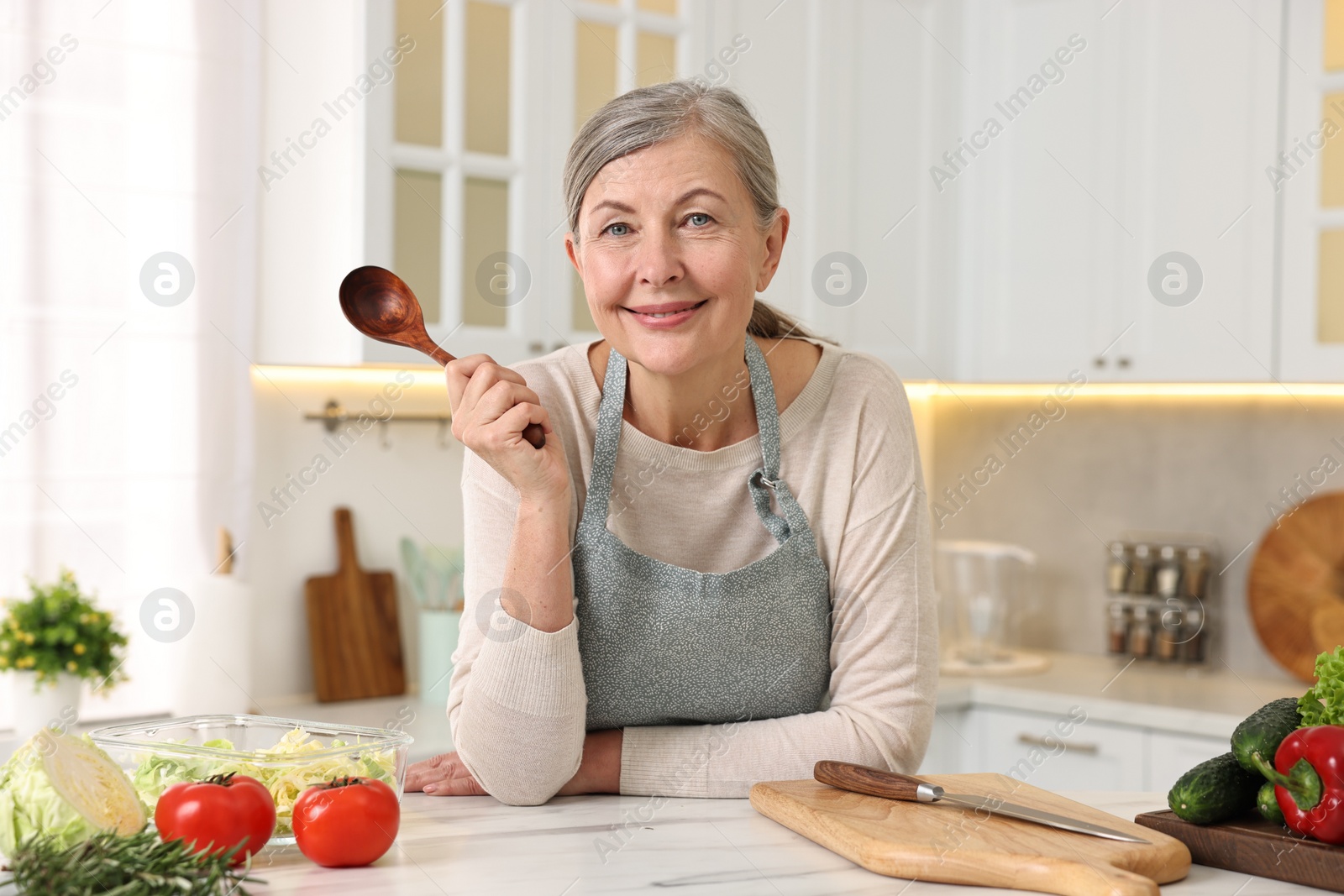 Photo of Happy housewife with spoon at white marble table in kitchen