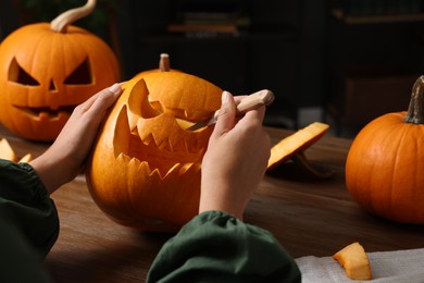 Photo of Woman carving pumpkin for Halloween at wooden table, closeup