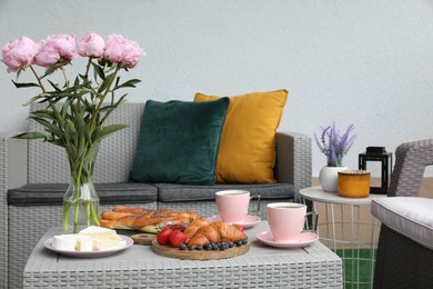 Photo of Morning drink, pastry, berries, cheese and vase with flowers on rattan table. Summer breakfast on terrace