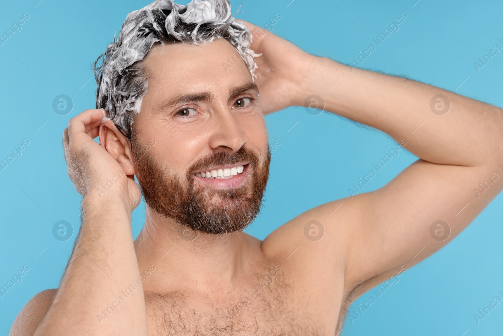 Photo of Happy man washing his hair with shampoo on light blue background, closeup