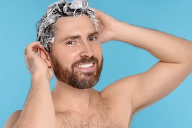 Photo of Happy man washing his hair with shampoo on light blue background, closeup