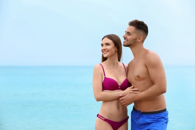 Young woman in bikini with her boyfriend on beach, space for text. Lovely couple