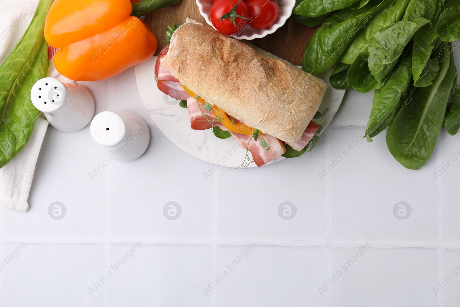 Photo of Tasty sandwich with bacon, tomatoes, greens and bell pepper on white tiled table, flat lay. Space for text