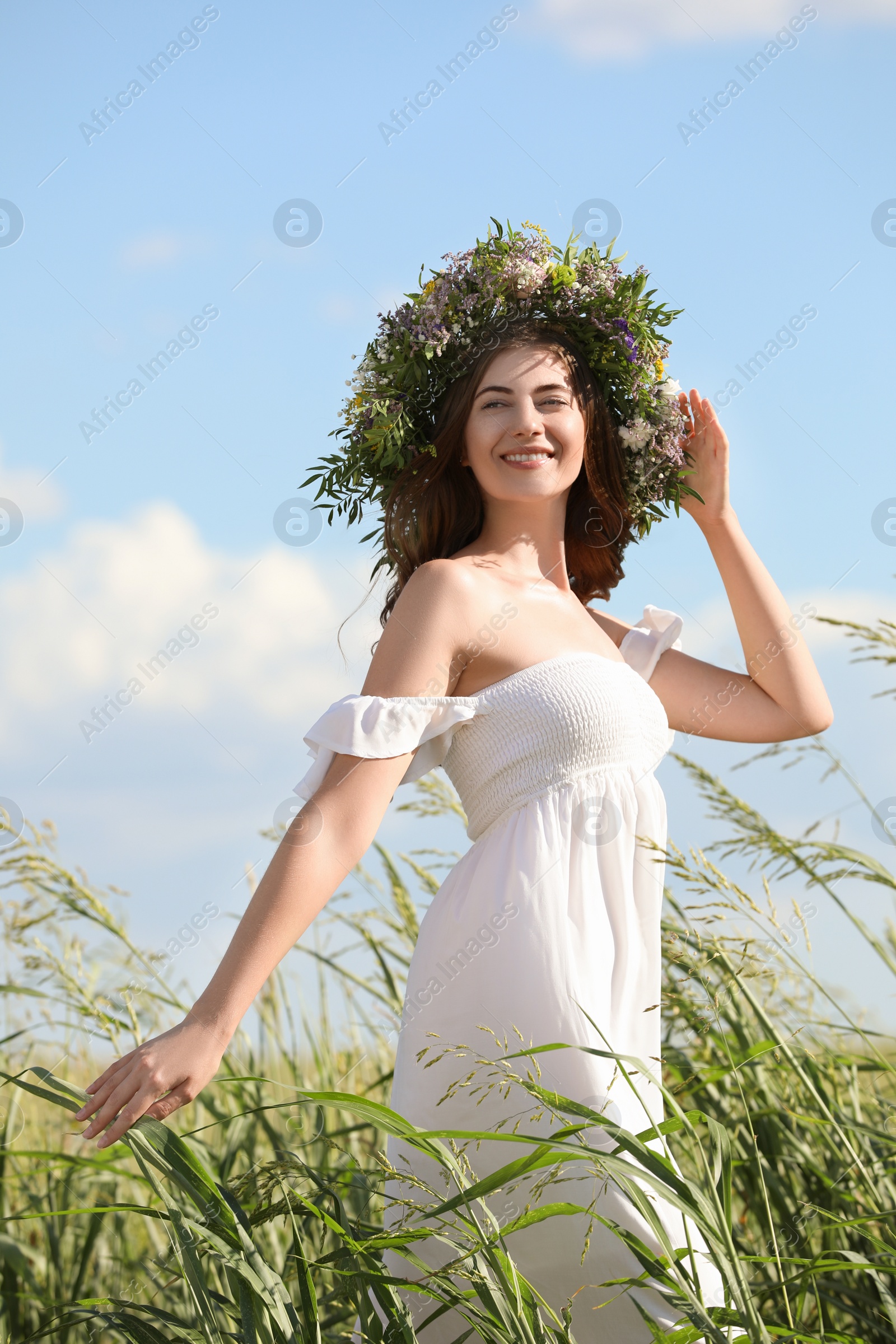 Photo of Young woman wearing wreath made of beautiful flowers in field on sunny day