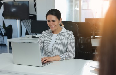 Happy woman working on laptop at white table in open plan office
