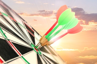 Dart board with color arrows hitting target against sunset sky