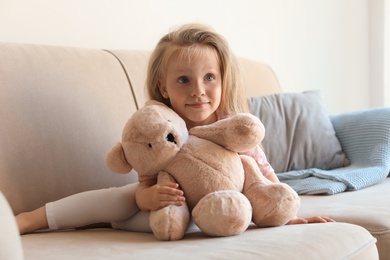 Cute little girl with teddy bear on sofa in room