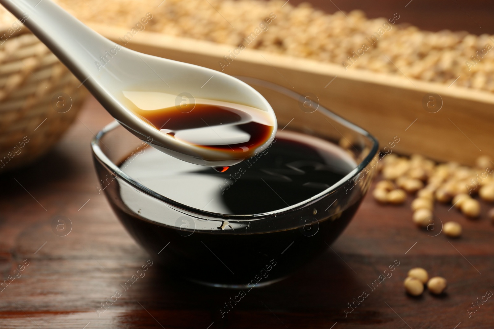 Photo of Taking soy sauce with spoon from bowl at wooden table, closeup