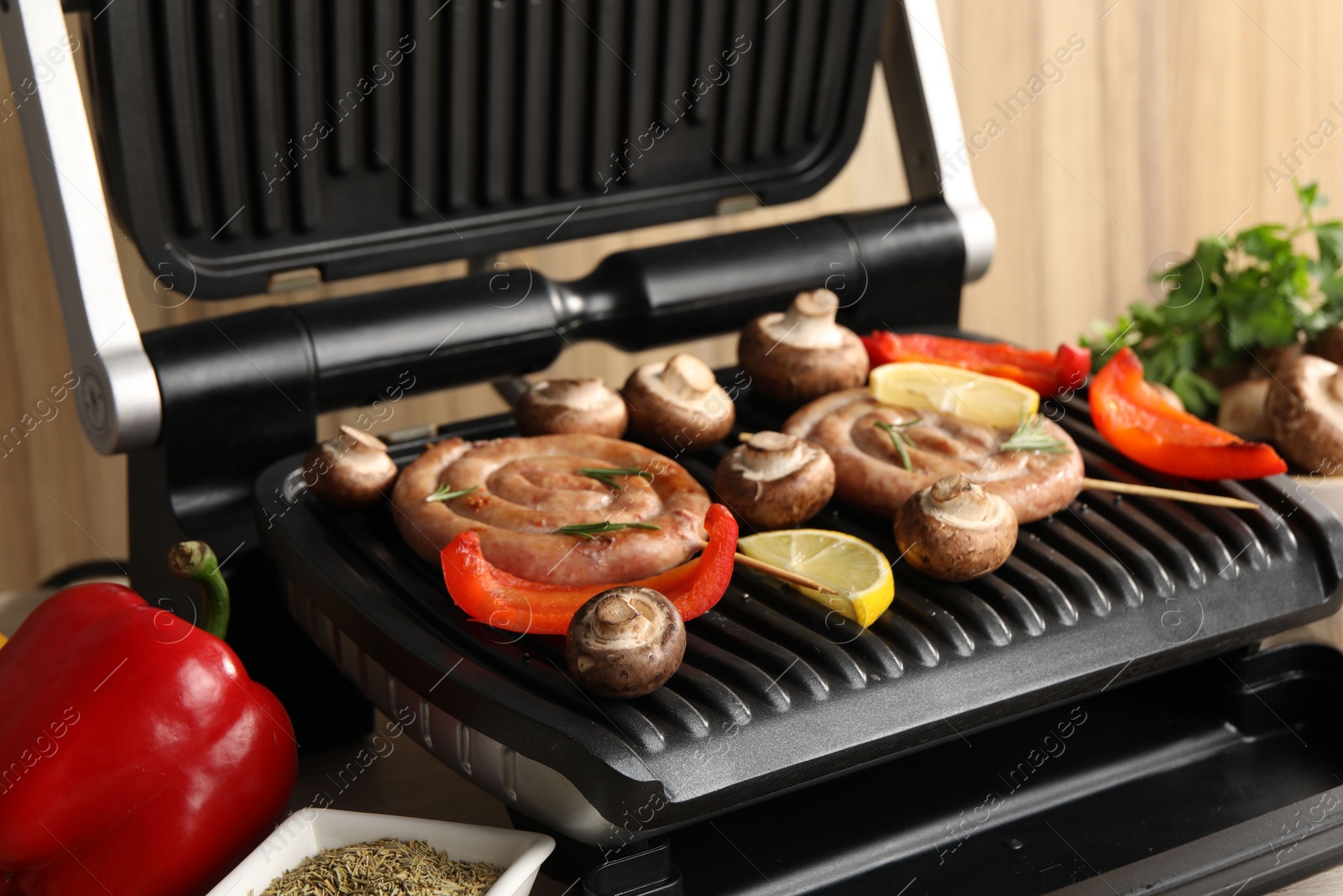 Photo of Electric grill with homemade sausages, mushrooms and bell pepper on table, closeup