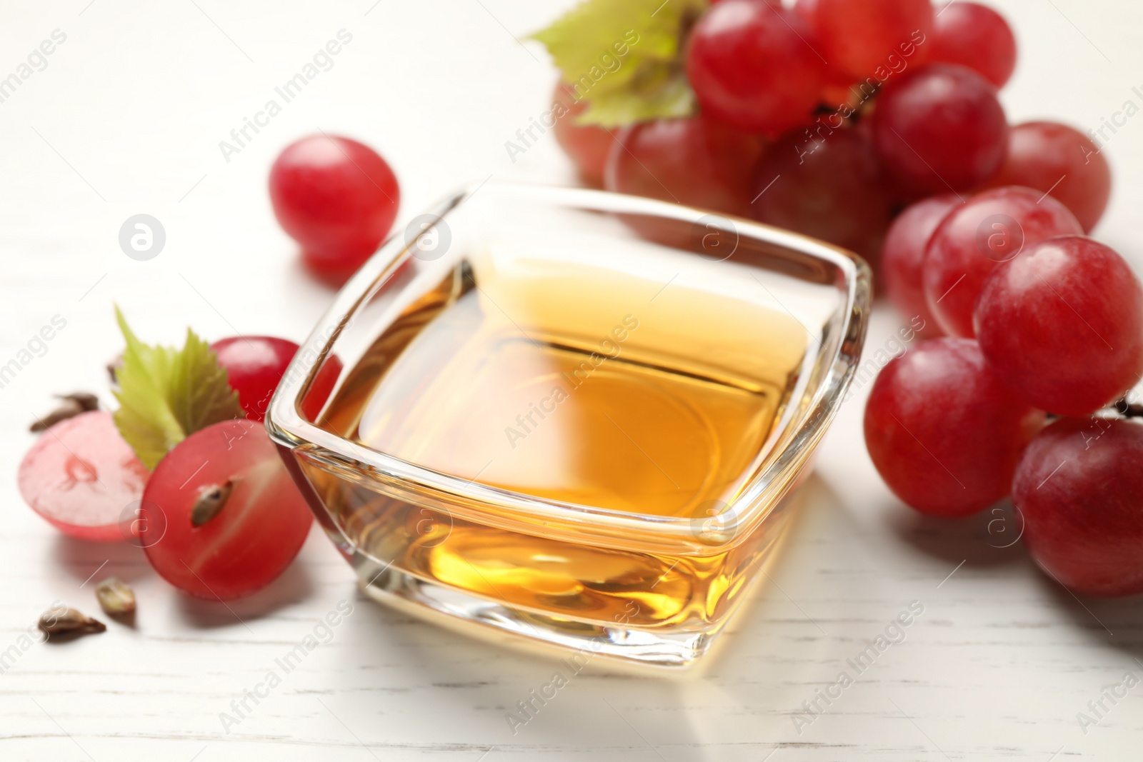 Photo of Glass bowl of natural grape seed oil on white wooden table. Organic cosmetic