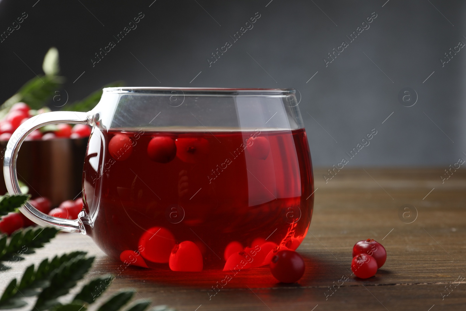 Photo of Tasty hot cranberry tea in glass and fresh berries on wooden table