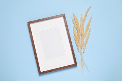 Photo of Empty photo frame and dry decorative spikes on light blue background, flat lay. Space for design