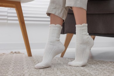 Photo of Woman wearing warm knitted socks at home, closeup. Space for text