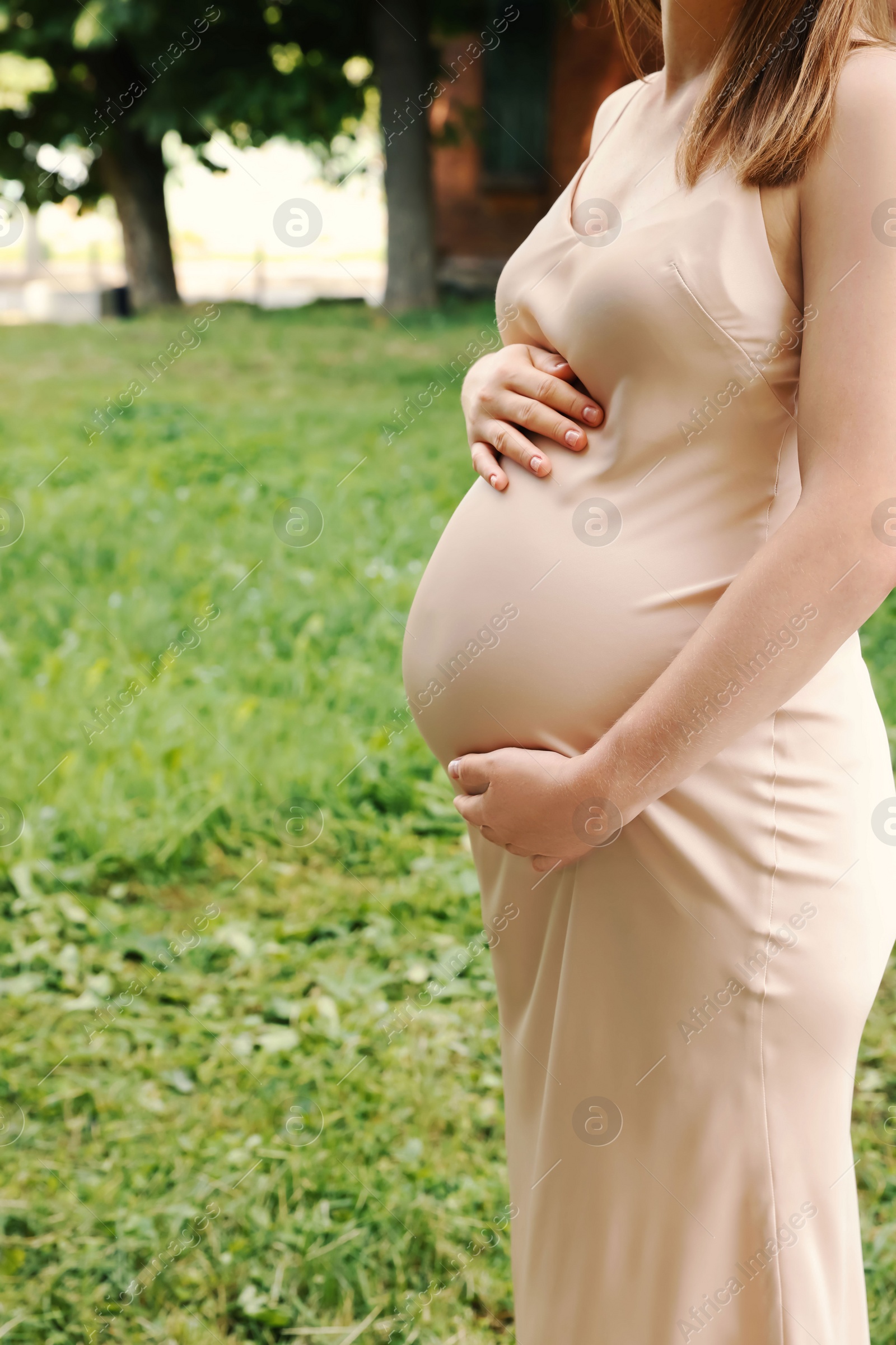 Photo of Pregnant woman touching belly outdoors, closeup view