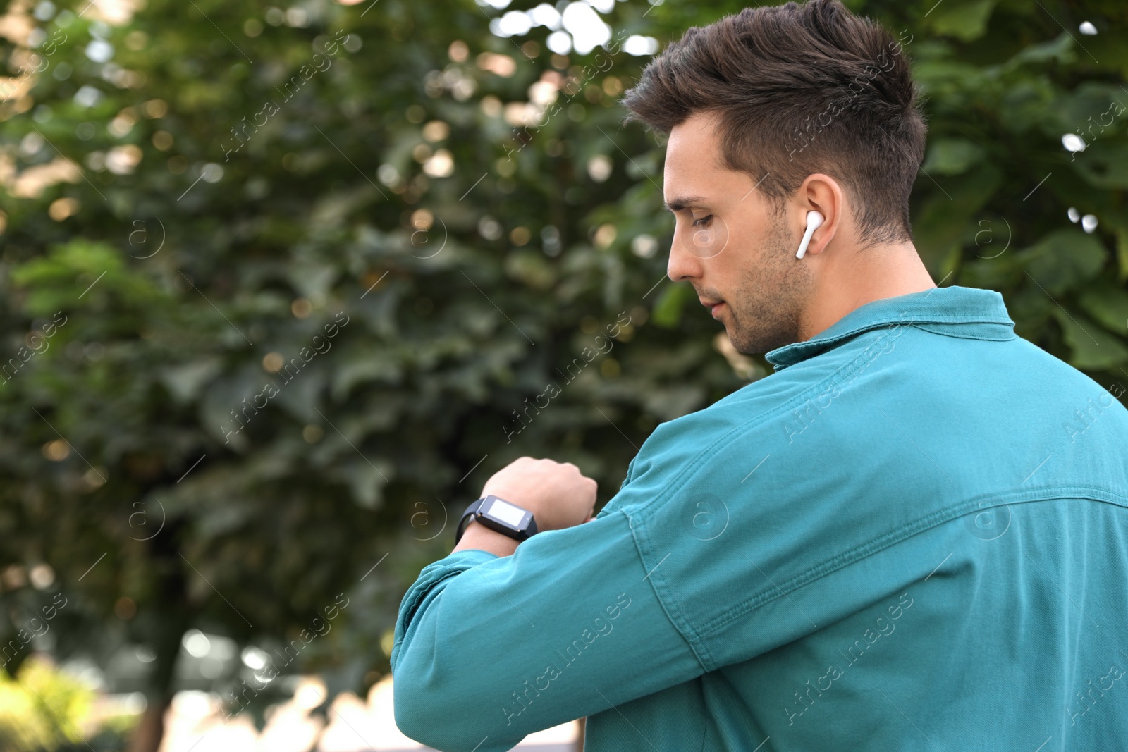 Photo of Young man with wireless earphones and smart watch in park