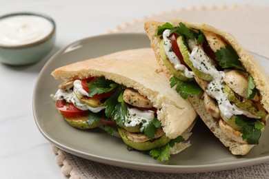 Photo of Delicious pita sandwiches with grilled vegetables and sour cream sauce on white table, closeup