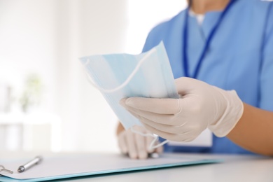 Photo of Doctor in medical gloves holding protective mask at table in office, closeup