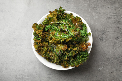 Photo of Tasty baked kale chips on grey table, top view