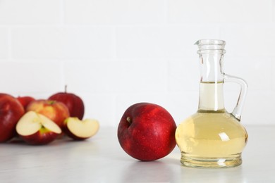 Photo of Natural apple vinegar and fresh fruits on white marble table. Space for text