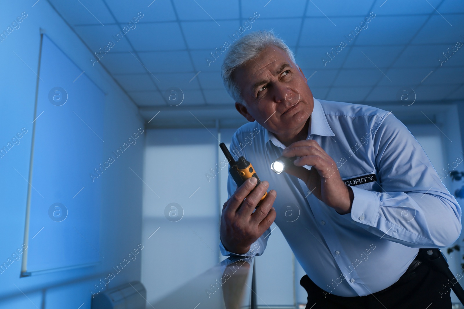 Photo of Professional security guard with portable radio set and flashlight in dark room