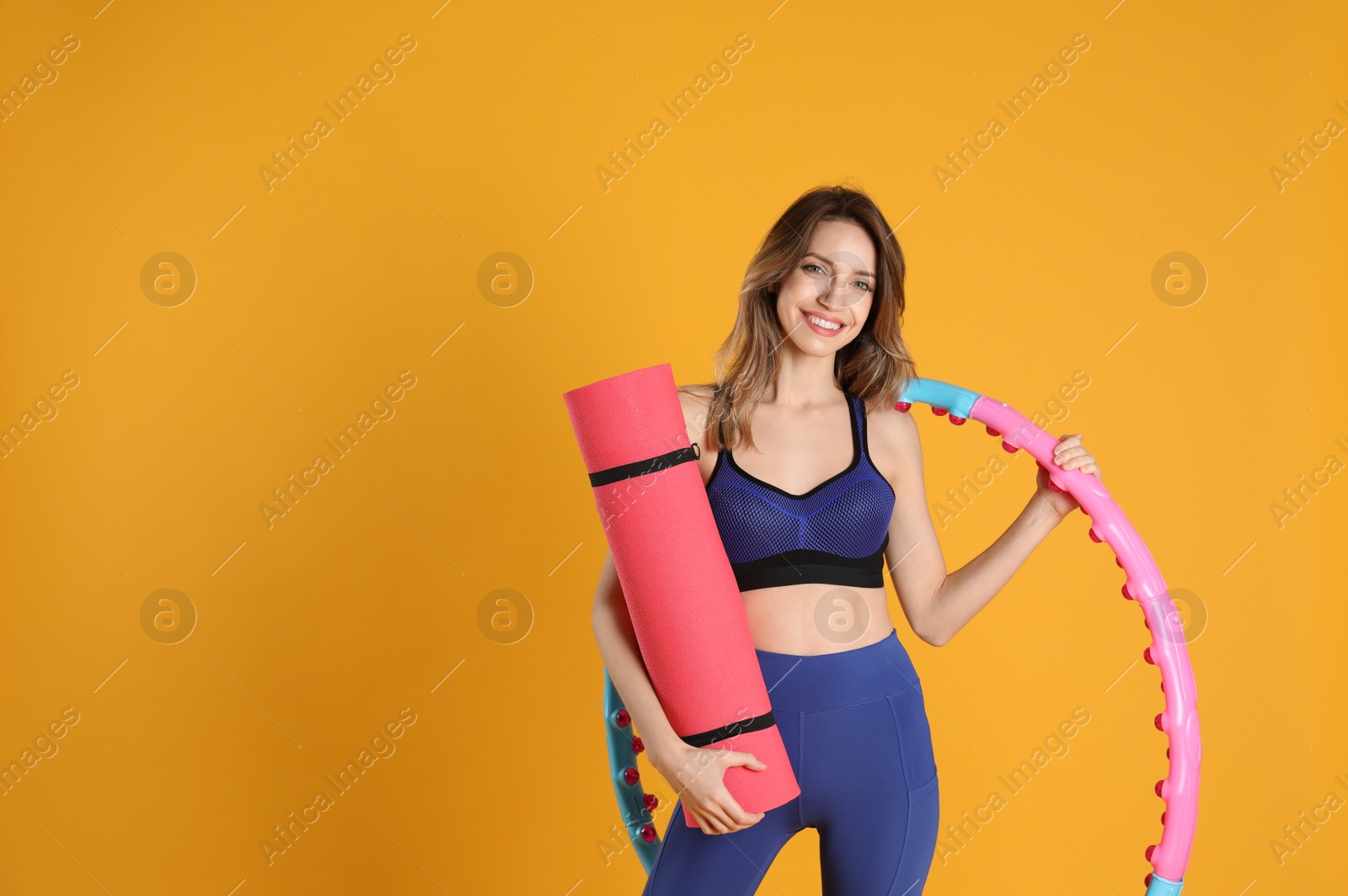 Photo of Beautiful  woman with yoga mat and hula hoop on yellow background