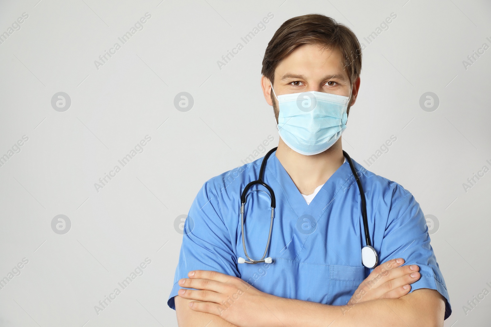 Photo of Doctor or medical assistant (male nurse) with protective mask and stethoscope on light grey background. Space for text