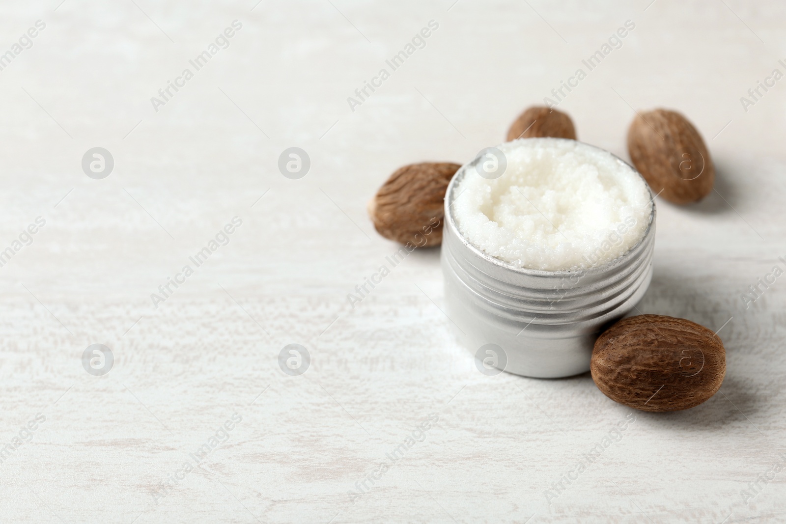 Photo of Shea butter in jar and nuts on white table. Space for text