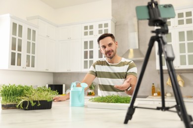 Photo of Teacher with microgreens and watering can conducting online course in kitchen. Time for hobby