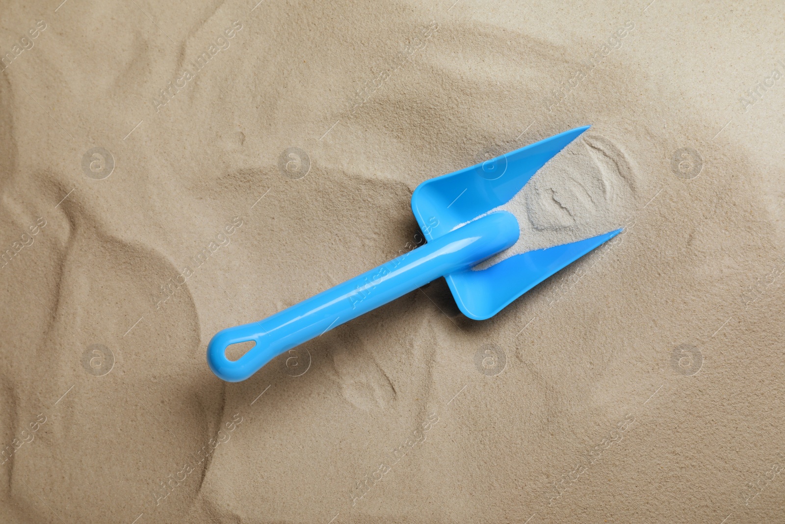 Photo of Bright plastic toy shovel on sand, top view