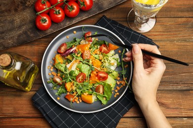Photo of Woman eating delicious salad with lentils and vegetables at wooden table, top view