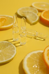 Skincare ampoules with vitamin C and citrus slices on yellow background