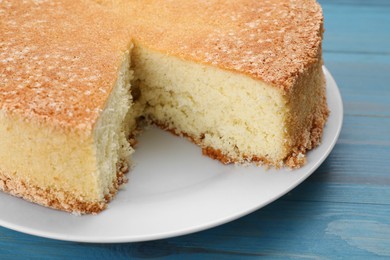 Plate with cut tasty sponge cake on light blue wooden table, closeup