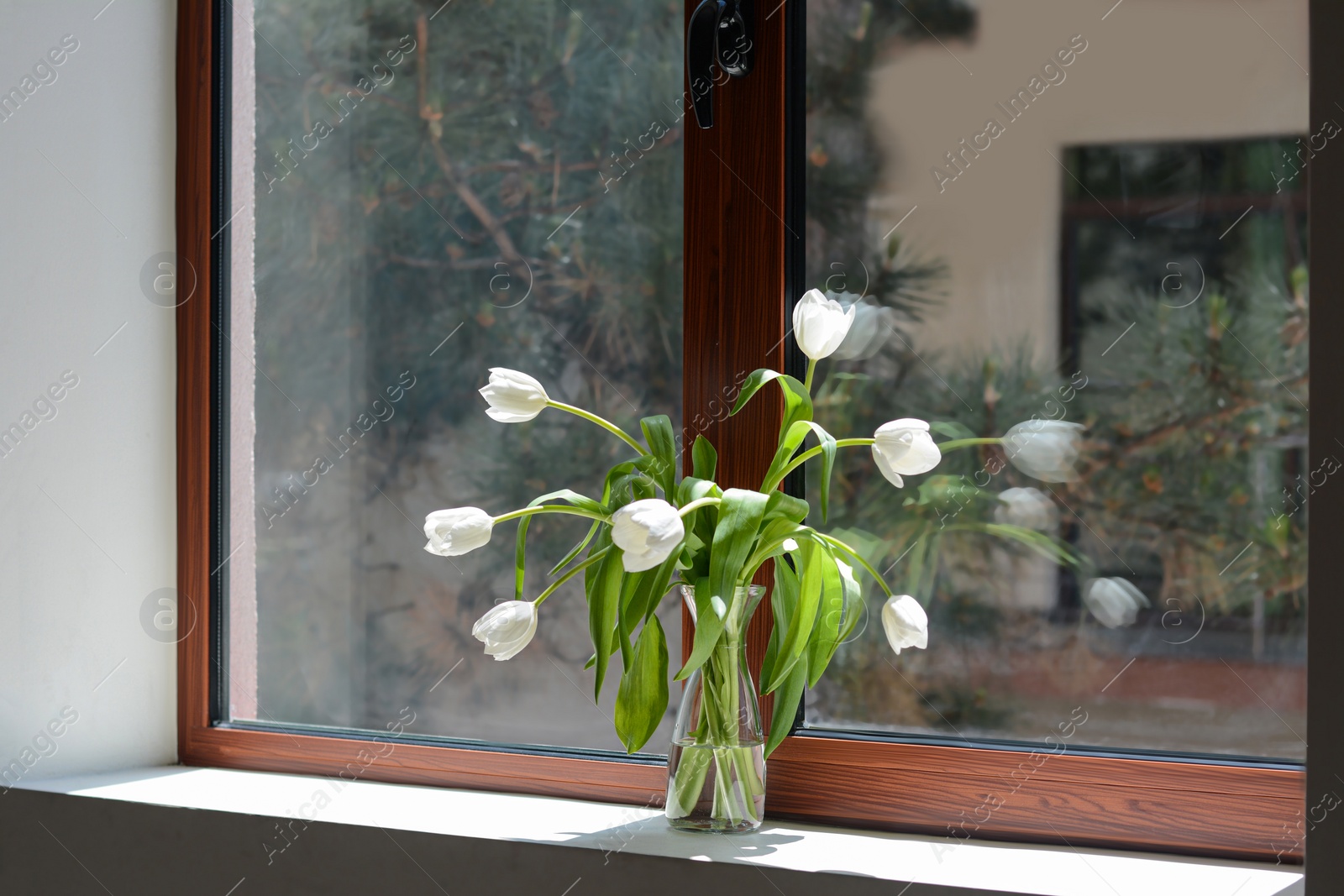 Photo of Bouquet of beautiful white tulip flowers in glass vase on windowsill indoors